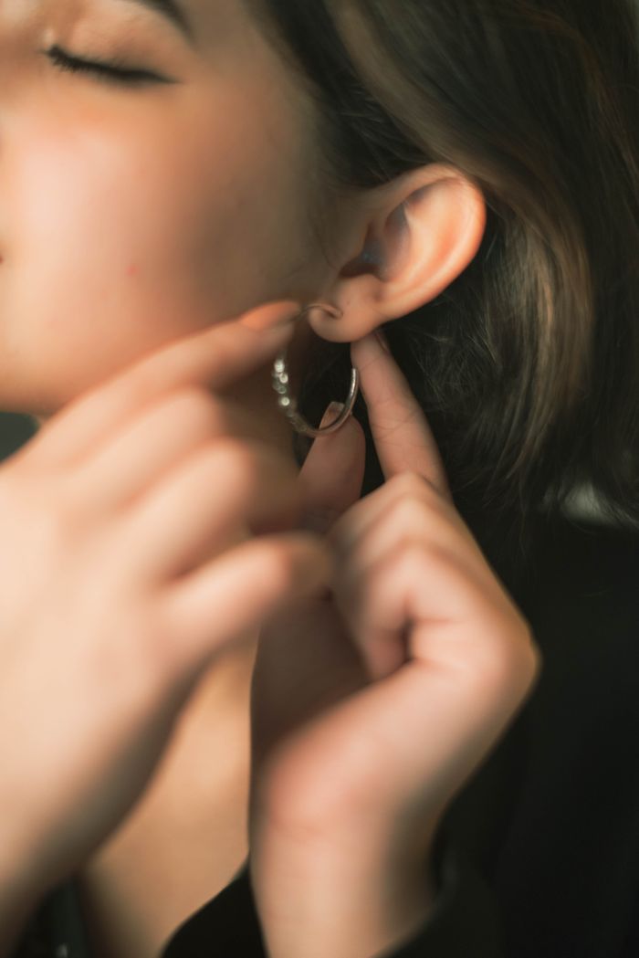 Close-up of a woman adjusting a silver hoop earring, capturing elegance and style.