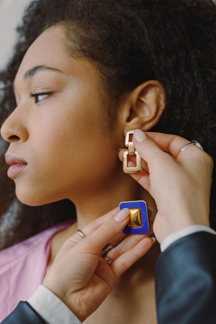 Close-up of a woman trying on gold geometric earrings with assistance, emphasizing modern fashion style.