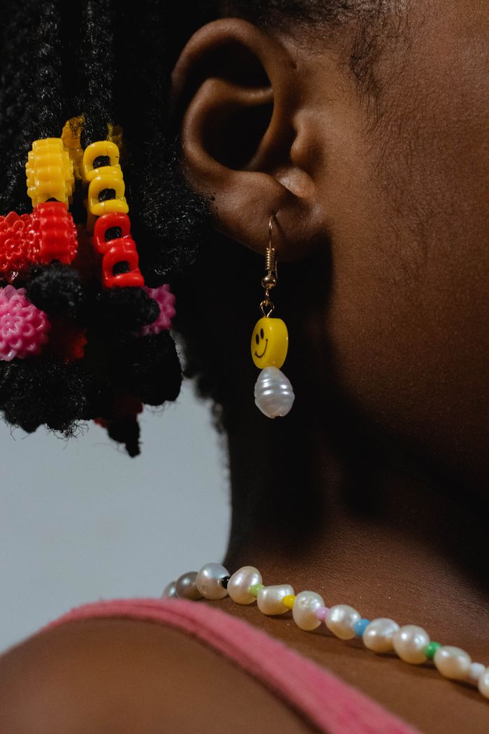 Detailed close-up of a child wearing colorful beads, a smiley earring, and a pearl necklace.